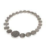 The escalator neckpiece shows geometric abstraction through its precisely offset tapering disc construction, the gently undulating surfaces create a dynamic interplay of light, while the oxidised recesses articulate the linear deconstructed form. Escalator neckpiece by Sarah Herriot.