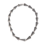 This striking neckpiece in silver showcases an inventive architectural approach to contemporary jewellery design, composed of linked pyramid forms, the piece uses linear deconstruction to create visual rhythm and movement. Oxidised recesses accentuate and amplifying the jazzy aesthetic, a bold statement piece for those seeking unconventional jewellery that challenges traditional forms whilst maintaining refined craftsmanship. Pyramid neckpiece by Sarah Herriot.