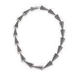 This striking neckpiece in silver showcases an inventive architectural approach to contemporary jewellery design, composed of linked pyramid forms, the piece uses linear deconstruction to create visual rhythm and movement. Oxidised recesses accentuate and amplifying the jazzy aesthetic, a bold statement piece for those seeking unconventional jewellery that challenges traditional forms whilst maintaining refined craftsmanship. Pyramid neckpiece by Sarah Herriot.