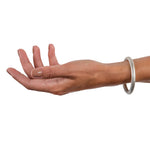 A masterfully engineered solid silver bangle with a seamless tension clasp that requires no visible mechanism. The round-section wire creates a refined, sculptural form that sits beautifully on the wrist with an authentic weight and presence. Seamless design embodies minimalist principles, pure form without ornamentation. Tension bangle by Sarah Herriot.
